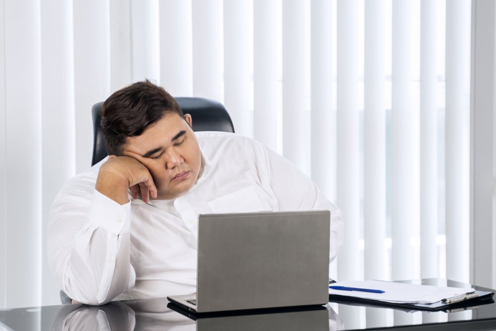 Übergewichtiger Mann schläft im Büro am Laptop